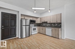 Kitchen featuring wood-finish flooring, light wood-look cabinetry, stainless steel refrigerator, white range, and white dishwasher - 