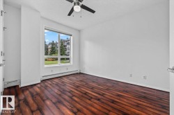 Spacious room featuring rich wood-finish flooring and a large window overlooking green space - 
