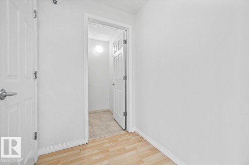 Interior entryway featuring light wood-finish flooring, white walls, and a white six-panel door with a brushed nickel lever handle - 116 6315 135 Avenue, Edmonton, AB 