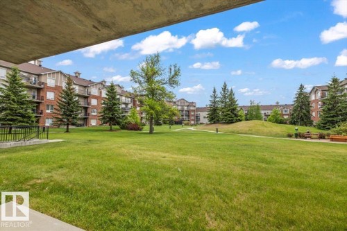 Expansive green space featuring mature trees and a manicured lawn, surrounded by multi-story residential buildings with brick and siding exteriors - 116 6315 135 Avenue, Edmonton, AB 