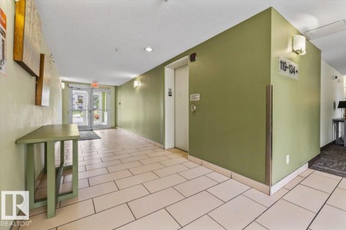 Hallway featuring neutral-toned tile flooring, recessed lighting, and wall-mounted sconces - 116 6315 135 Avenue, Edmonton, AB 