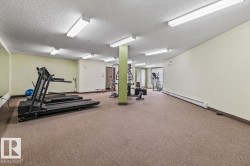 Carpeted fitness area featuring multiple fluorescent light fixtures, a mirrored wall section, and a full-light glass panel door - 