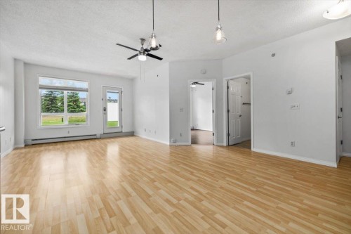 Spacious living area featuring light wood-finish flooring, white walls, and a textured ceiling - 116 6315 135 Avenue, Edmonton, AB 