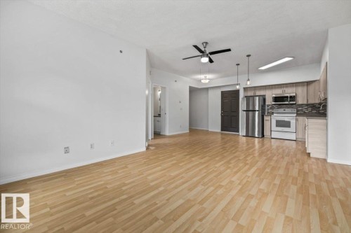 Open-concept living space featuring wood-finish flooring, a kitchen with stainless steel appliances, light wood-finish cabinetry, and a dark tile backsplash - 116 6315 135 Avenue, Edmonton, AB 