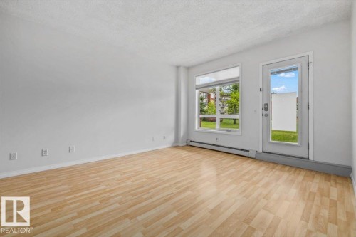 Spacious room featuring wood-finish flooring, white walls, and a large window with a glass-paneled door - 116 6315 135 Avenue, Edmonton, AB 