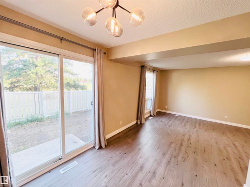 Spacious room featuring wood-finish flooring, a contemporary ceiling light fixture, sliding glass doors to a concrete patio, and a window with natural light - 2544 79 Street, Edmonton, AB - Indoor Photo Showing Other Room
