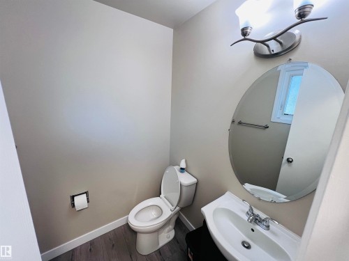 Powder room featuring a circular wall mirror, a single-basin sink, and overhead brushed nickel lighting - 2544 79 Street, Edmonton, AB - Indoor Photo Showing Bathroom