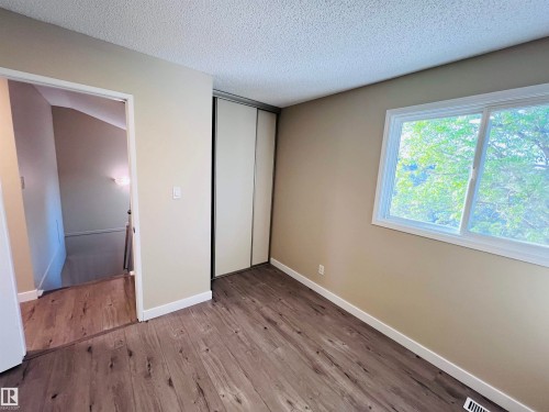 Room featuring wood-finish flooring, a large window, bi-fold closet doors, and light beige wall paint - 2544 79 Street, Edmonton, AB - Indoor Photo Showing Other Room