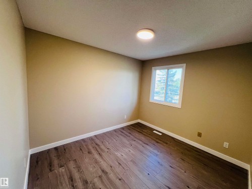 Spacious room featuring wood-finish flooring, neutral-toned walls, a white trim window, and a flush-mount ceiling light fixture - 2544 79 Street, Edmonton, AB - Indoor Photo Showing Other Room