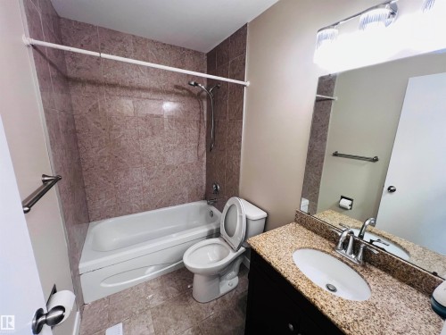 Bathroom featuring a combination shower and tub with full-height tile surround, dark wood-finish vanity with a light-toned stone countertop, and an oval undermount sink - 2544 79 Street, Edmonton, AB - Indoor Photo Showing Bathroom