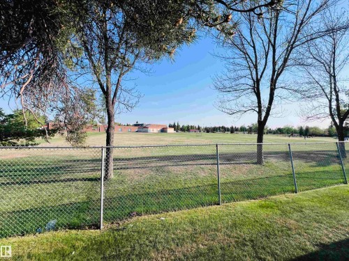 Expansive green space featuring a chain-link fence, mature trees, and a distant building with a brick exterior - 2544 79 Street, Edmonton, AB - Outdoor With View