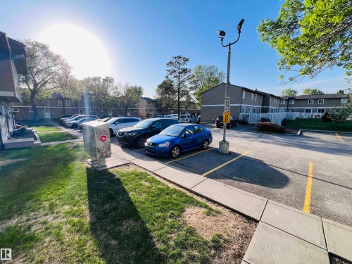 Paved parking area with marked spaces and street lighting, bordered by a concrete sidewalk and green lawn - 2544 79 Street, Edmonton, AB - Outdoor