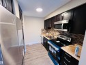 Kitchen featuring dark wood-finish cabinetry with silver hardware, stainless steel appliances, a multi-tone tile backsplash, light wood-finish countertops, and wood-finish flooring - 2544 79 Street, Edmonton, AB  - Indoor Photo Showing Kitchen With Double Sink 