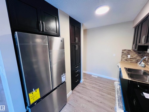 Kitchen featuring stainless steel appliances, dark cabinetry with bar pull hardware, wood-finish flooring, a mosaic tile backsplash, and a double basin sink - 2544 79 Street, Edmonton, AB - Indoor Photo Showing Kitchen With Double Sink