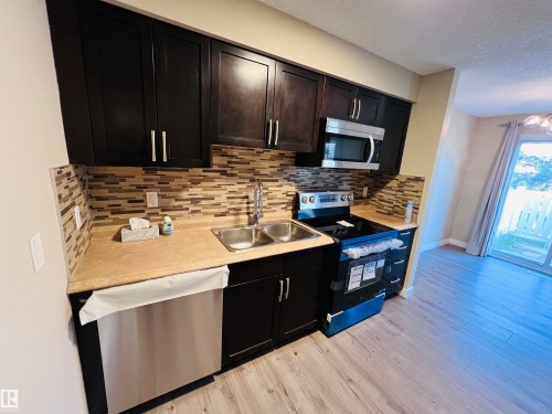 Kitchen featuring dark wood-finish cabinetry, stainless steel appliances, a mosaic tile backsplash, and light wood-finish flooring - 2544 79 Street, Edmonton, AB - Indoor Photo Showing Kitchen With Double Sink With Upgraded Kitchen