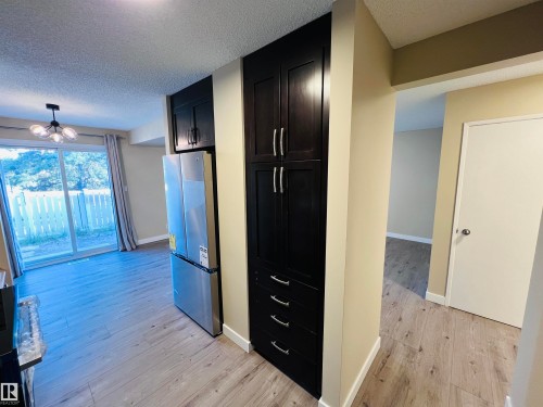 Kitchen featuring dark wood-finish cabinetry with silver hardware, stainless steel refrigerator, and wood-finish flooring - 2544 79 Street, Edmonton, AB - Indoor Photo Showing Other Room