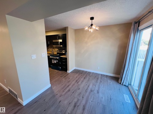 Open-concept living space featuring wood-finish flooring, a modern multi-bulb chandelier, and warm neutral wall tones - 2544 79 Street, Edmonton, AB - Indoor Photo Showing Other Room
