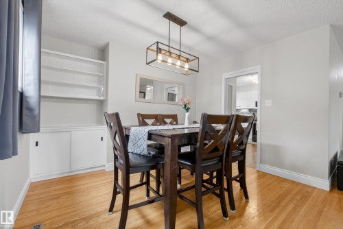 Dining area featuring wood-finish flooring, built-in shelving with lower cabinetry, and a contemporary linear chandelier - 16105 109A Avenue, Edmonton, AB 