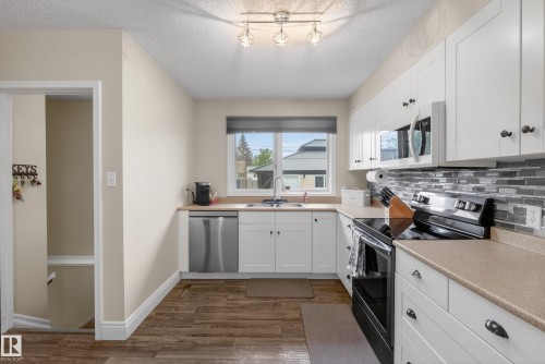 Kitchen featuring white cabinetry, dark wood-finish flooring, and a multi-tone tile backsplash - 16105 109A Avenue, Edmonton, AB 