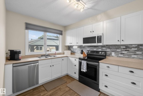 Well-appointed kitchen featuring white cabinetry, a stainless steel dishwasher, a black range, and a multi-tone tile backsplash - 16105 109A Avenue, Edmonton, AB 