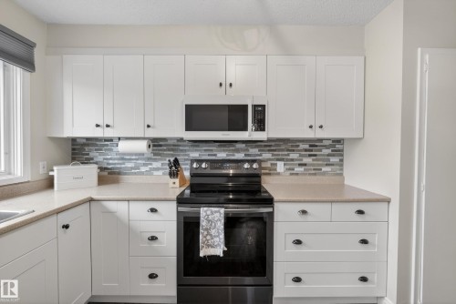 Kitchen featuring white shaker-style cabinetry, a multi-tone tile backsplash, and light-toned countertops - 16105 109A Avenue, Edmonton, AB 