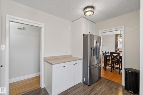 Modern kitchen area featuring wood-finish flooring, stainless steel French door refrigerator, white cabinetry with dark hardware, and a light-toned countertop - 16105 109A Avenue, Edmonton, AB 