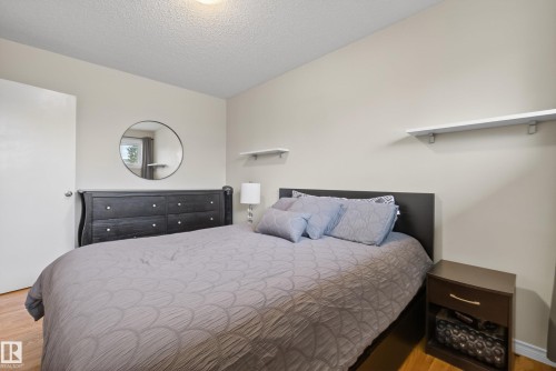 Bedroom featuring light-toned walls, wood-finish flooring, a contemporary ceiling light fixture, and white accent shelving - 16105 109A Avenue, Edmonton, AB 