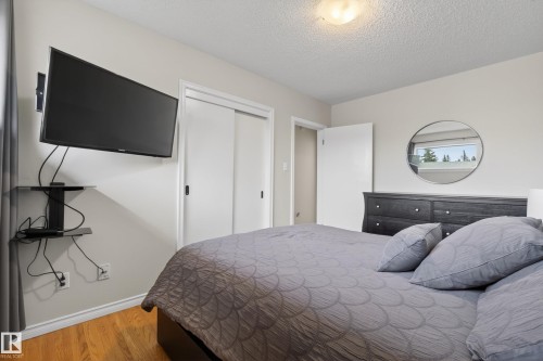 Bedroom featuring wood-finish flooring, a built-in closet with sliding doors, and a wall-mounted fixture - 16105 109A Avenue, Edmonton, AB 