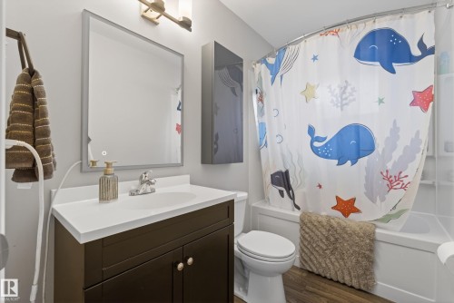 Bathroom featuring a dark wood-finish vanity, a white countertop with an integrated sink, a rectangular framed mirror with integrated lighting, a wall-mounted medicine cabinet, and a white bathtub - 16105 109A Avenue, Edmonton, AB 