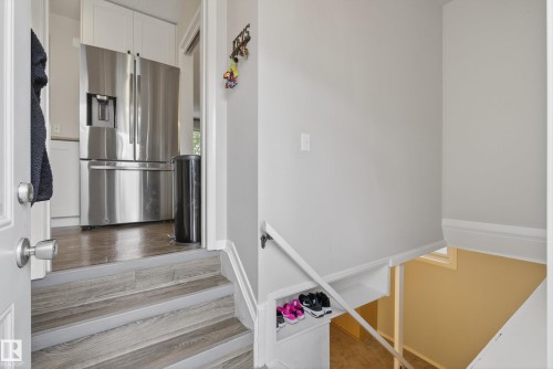 Split-level entry with wood-finish stairs, stainless steel French door refrigerator, white shaker-style cabinetry, and wood-finish flooring - 16105 109A Avenue, Edmonton, AB 