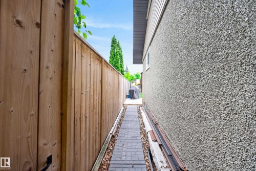 Side yard access featuring a wood privacy fence, textured exterior wall, and paver pathway - 16105 109A Avenue, Edmonton, AB 