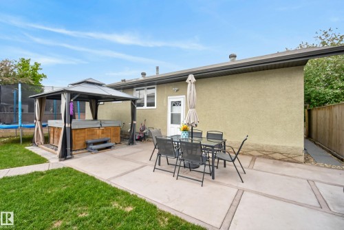 Expansive concrete patio area with a covered hot tub, offering multiple zones for outdoor enjoyment - 16105 109A Avenue, Edmonton, AB 