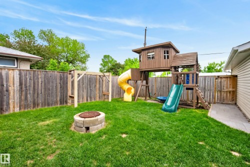 Fenced backyard featuring a wood playset with yellow and green slides, a swing set structure, a stone fire pit, and a paver pathway - 16105 109A Avenue, Edmonton, AB 