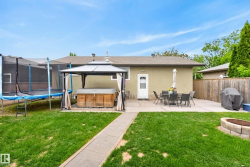 Expansive backyard featuring a concrete patio, a covered gazebo housing a hot tub, and a separate fire pit area with stone block surround - 16105 109A Avenue, Edmonton, AB 