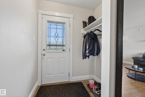 Entryway featuring a white door with decorative glass inserts, wood-finish flooring, and crisp white baseboards - 16105 109A Avenue, Edmonton, AB 