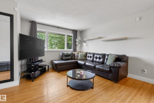 Spacious living area featuring light wood-finish flooring, a large window with natural light, and light gray wall paint - 16105 109A Avenue, Edmonton, AB 