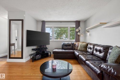 Living area featuring wood-finish flooring, a large window with exterior views, and a wall-mounted full-length mirror - 16105 109A Avenue, Edmonton, AB 