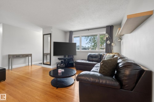Living area featuring wood-finish flooring, light-colored walls, a large window with exterior views, and floating wall shelves - 16105 109A Avenue, Edmonton, AB 