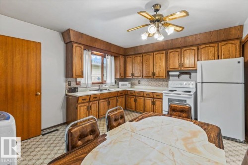 Kitchen featuring wood cabinetry, laminate countertops, a ceiling fan with integrated lighting, and white appliances including a range and refrigerator - 12923 113A Street, Edmonton, AB 