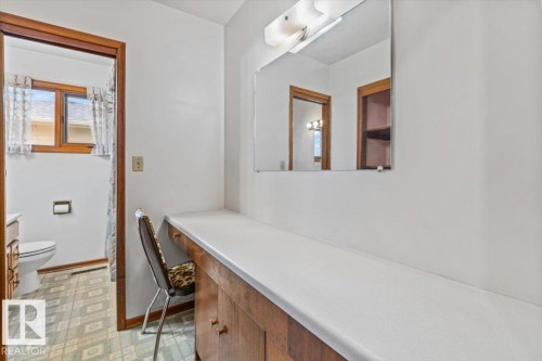 Integrated vanity with wood-finish cabinetry, a white countertop, and an overhead mirror with a light fixture - 12923 113A Street, Edmonton, AB 