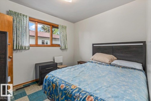 Bedroom featuring a wood-framed window, neutral wall paint, and a patterned floor with blue and beige squares - 12923 113A Street, Edmonton, AB 