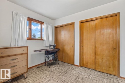 Bright room featuring a window with wood framing, two sliding wood closet doors, and patterned flooring - 12923 113A Street, Edmonton, AB 