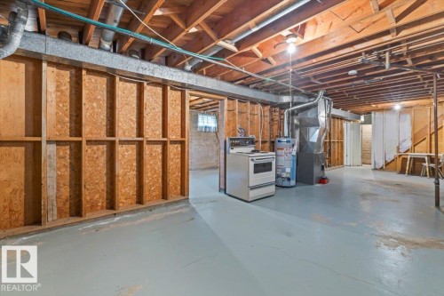 Unfinished basement space featuring exposed wood joists and structural beams, a painted concrete floor, and framed partition walls - 12923 113A Street, Edmonton, AB 