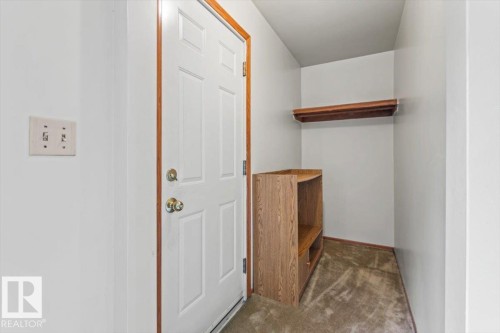 Entryway with a white paneled door featuring brass hardware, wood trim, and a wall-mounted light switch - 12923 113A Street, Edmonton, AB 