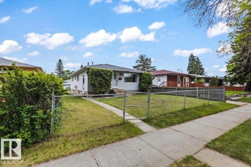 White ranch-style home featuring a gray shingle roof, a large front window, and mature landscaping - 12923 113A Street, Edmonton, AB 