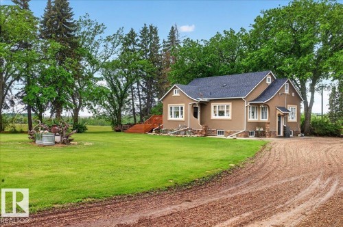 Stucco exterior residence featuring a dark shingle roof, white trim accents, and stone detailing around the foundation - 572004 Highway 857, Rural Two Hills County, AB 