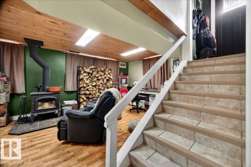 Wood-finish flooring and a wood-paneled ceiling define this lower-level area, featuring a black cast-iron wood-burning stove with a stone hearth - 572004 Highway 857, Rural Two Hills County, AB 