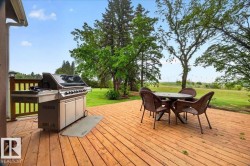 Expansive wooden deck featuring horizontal railings, ample space for outdoor dining, and a verdant lawn backdrop with mature trees - 