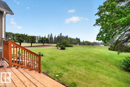 Expansive green lawn with scattered trees and a distant building, featuring a rustic wood deck with railings and integrated post lighting - 572004 Highway 857, Rural Two Hills County, AB 