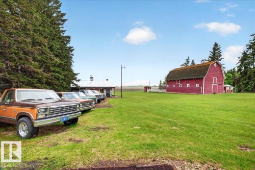 Expansive green lawn with a large red barn featuring a gambrel roof and multiple windows - 572004 Highway 857, Rural Two Hills County, AB 
